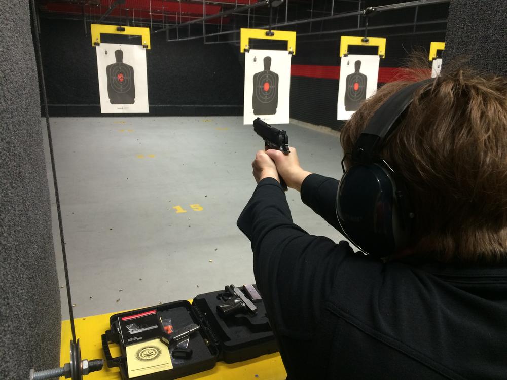 person wearing a black long sleeve shirt and ear protectors shooting a pistol at a paper target