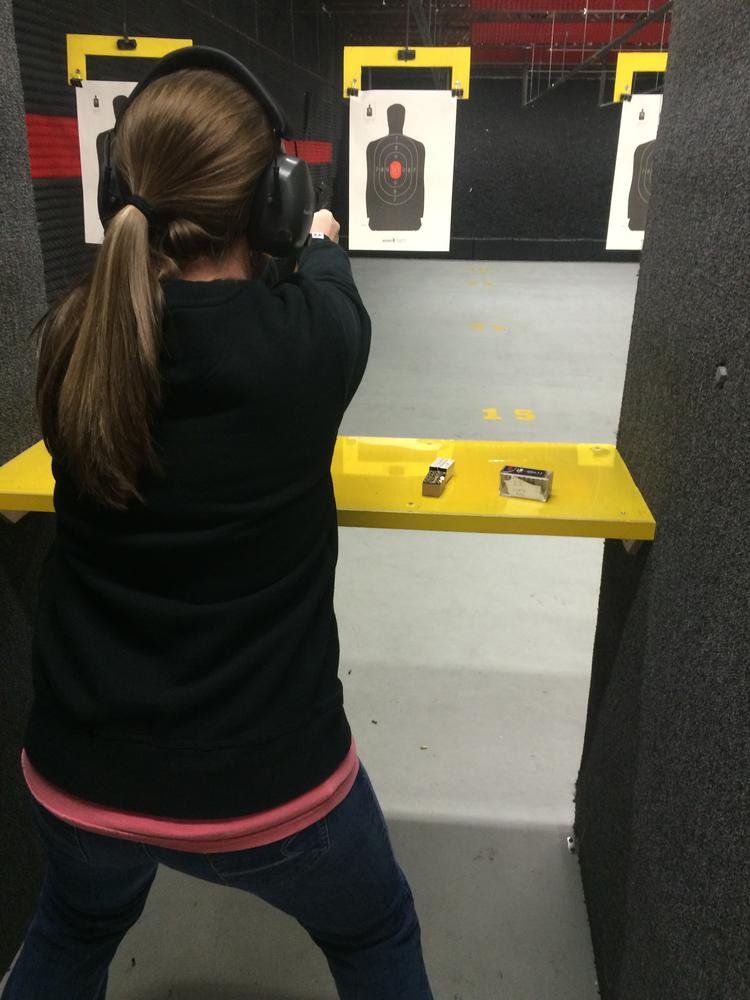 person in a long sleeve black shirt with black ear protectors looking at a paper target of a person