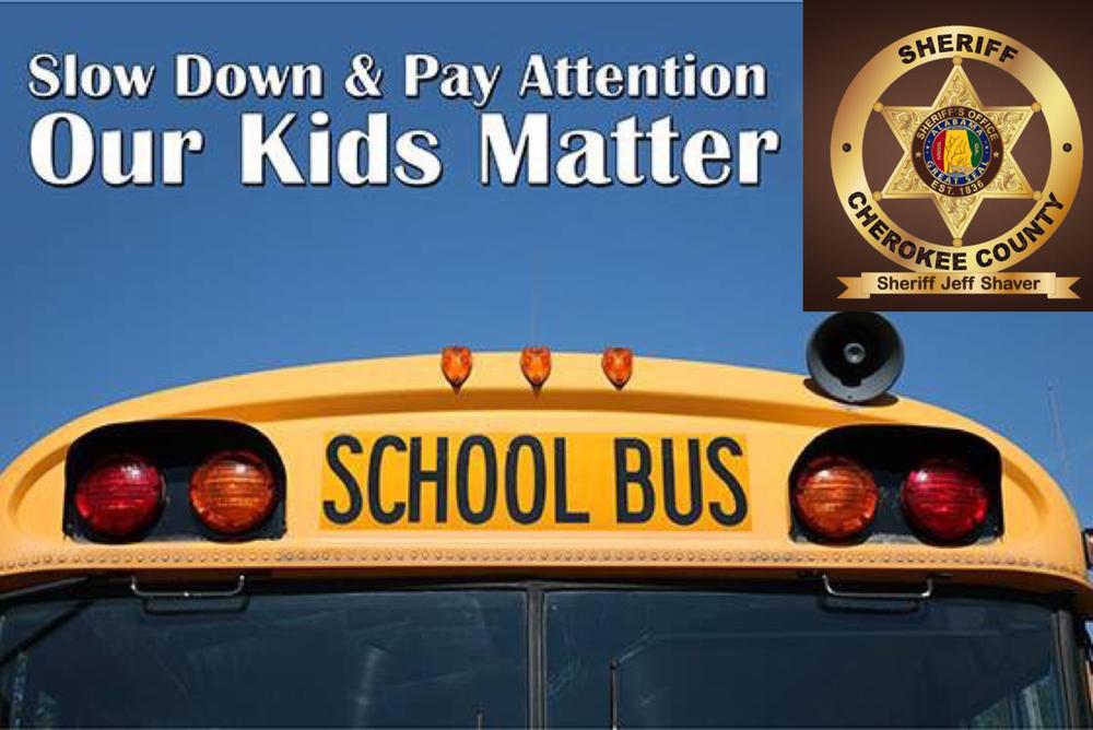 front of a school bus with slow down & pay attention our kids matter in white text and a gold sheriff of cherokee county badge
