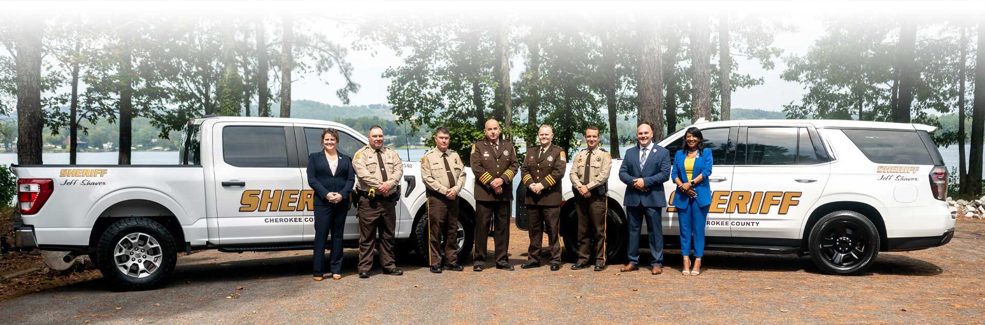 Cherokee County Sheriffs Office staff standing in front of patrol vehicles parked in front of trees