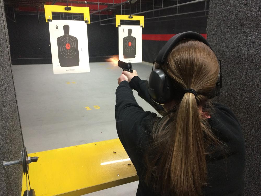 person with a long brown pony tail and black long sleeve shirt pointing a handgun at a paper target of a person