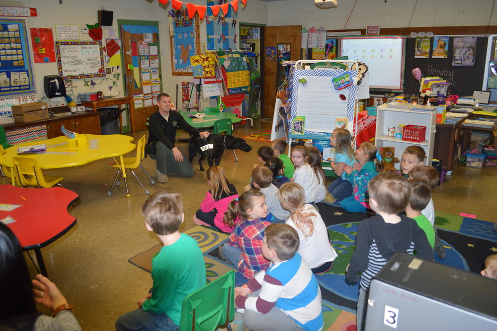 a group of kindergarten students sitting a the floor watching Deputy Michael Green and Keelo