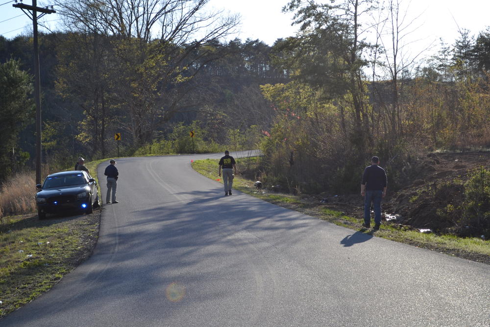 4 men in gray pants and black shirts walking along a road