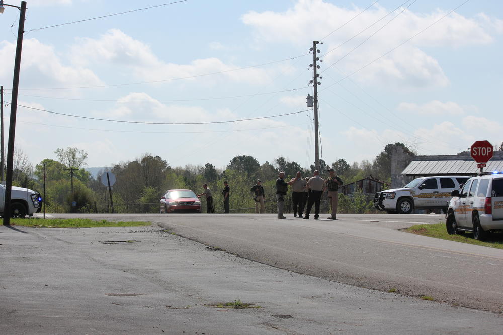 7 members of the Cherokee County Sheriff office stand in the road performing a traffic stop on a red car