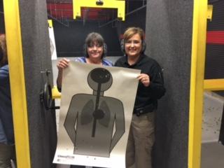 instructor standing with her student while holding her target from shooting at the firearms range