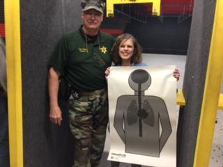 instructor standing with his student while holding her target from shooting at the firearms range