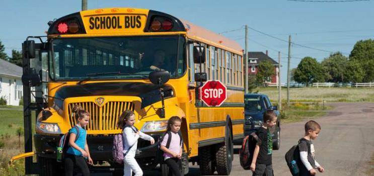 5 children walking in front of a yellow school bus with the red stop sign showing