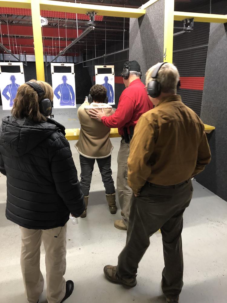 student being instructed how to use a firearm while 2 people watch